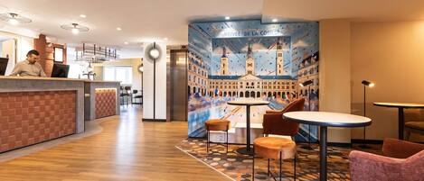 A hotel lobby with a reception desk, seating area, and a mural of a cityscape.