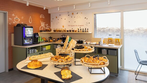 Un buffet de petit-déjeuner proposant du pain, des viennoiseries et des distributeurs de jus de fruits.