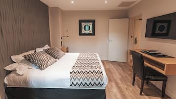 A bedroom with a bed, a desk, and a chair. There is a door and a wall-mounted picture.
