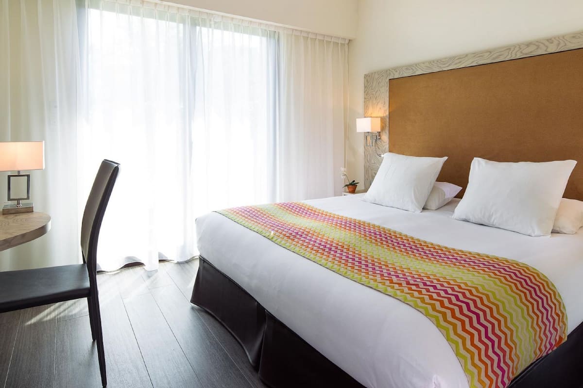 A hotel room with a bed, a desk, a chair, and a window with curtains.