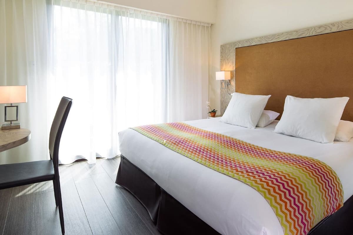 A hotel room with a bed, a desk, a chair, and a window with curtains.