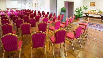 Une salle de conférence avec des rangées de chaises rouges et une table en bois sur laquelle sont disposés de la nourriture et des boissons.