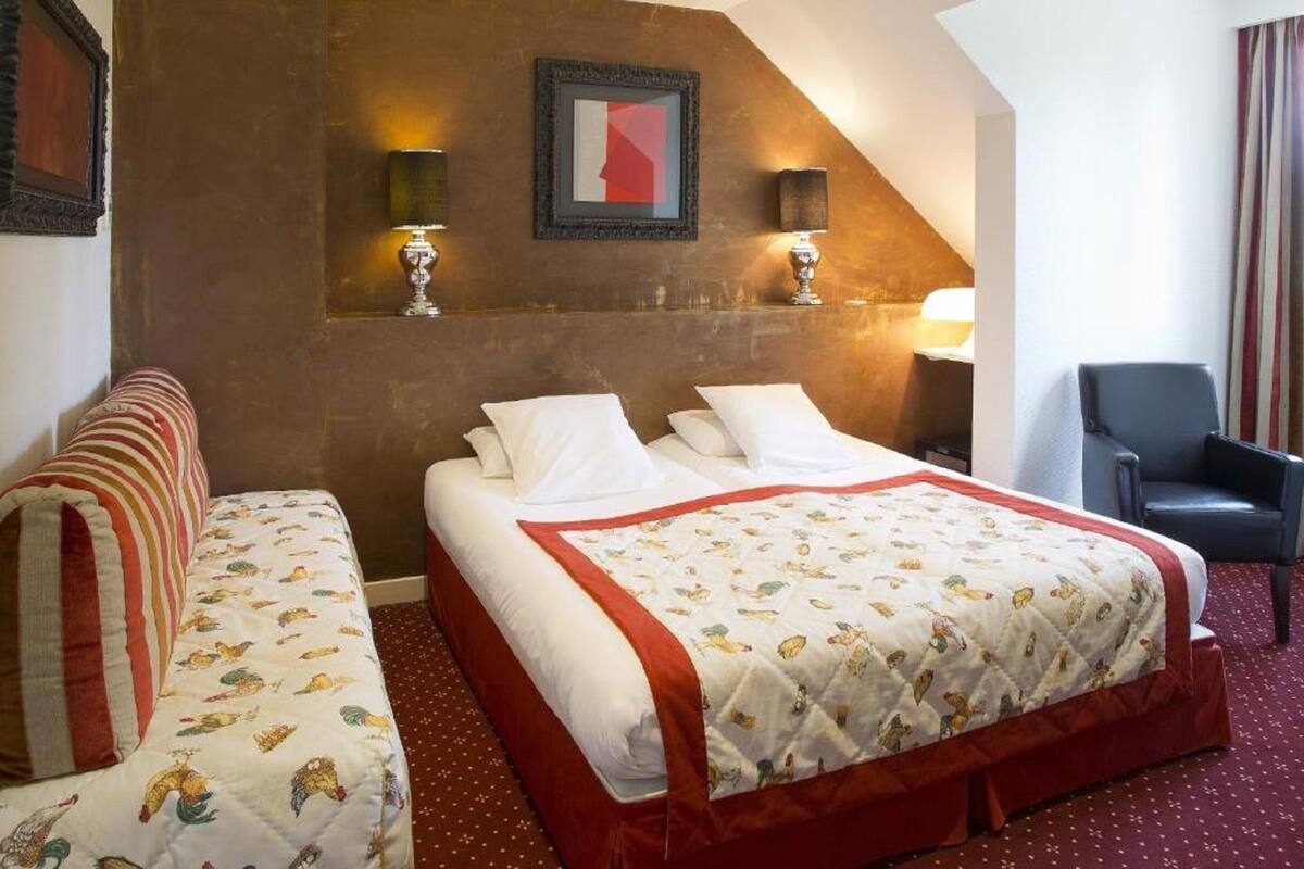 A hotel room with a bed, a sofa, a chair, and two wall-mounted lamps.