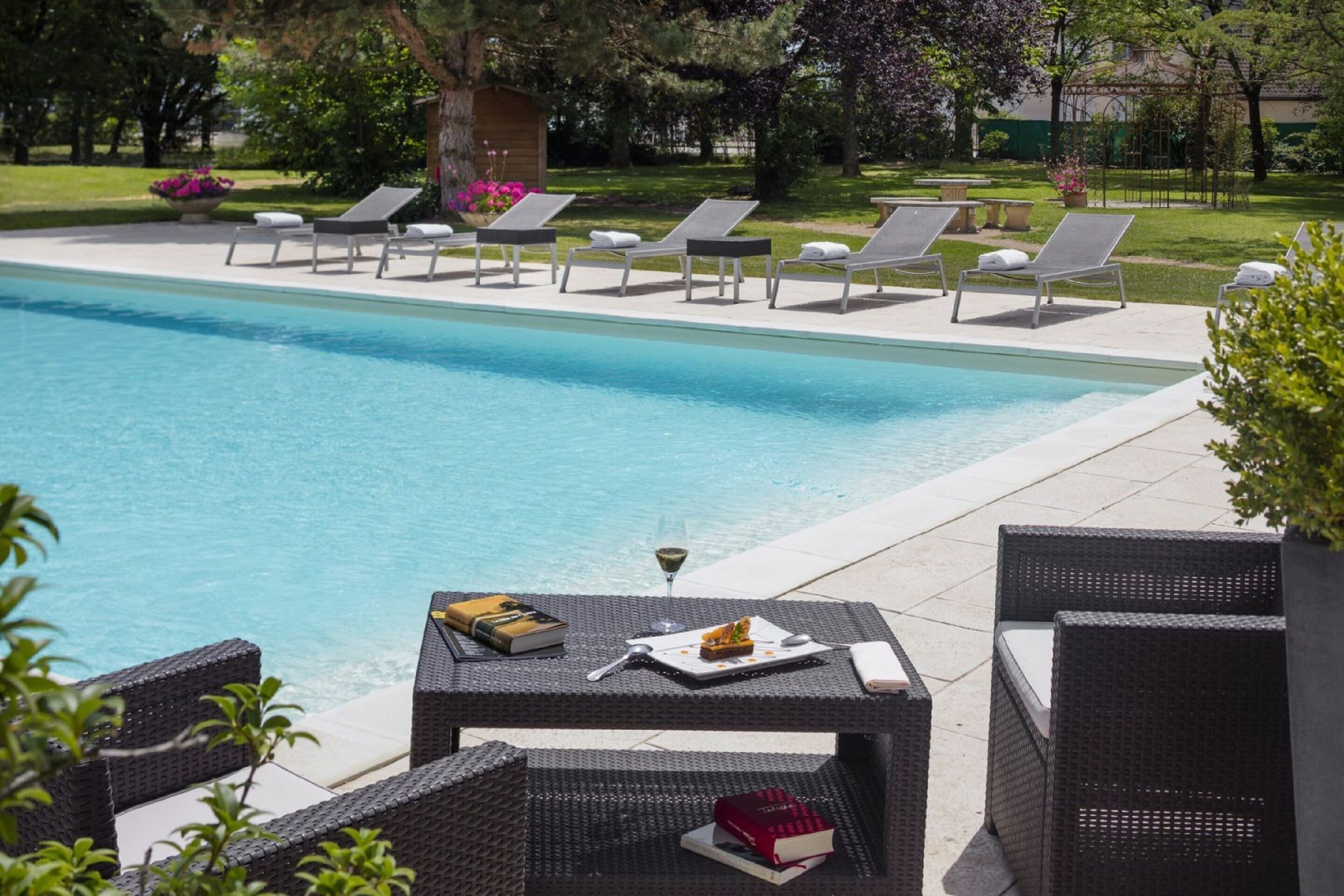 A swimming pool with lounge chairs and a table with books and a glass of wine.