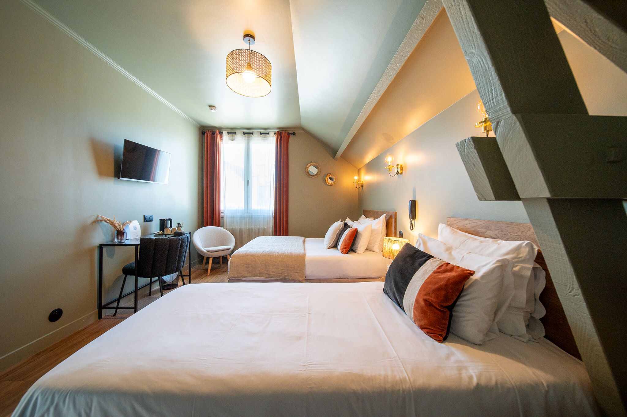 Ein Hotelzimmer mit zwei Betten, einem Schreibtisch, einem Stuhl, einem Fernseher und einem Fenster mit Vorhängen.