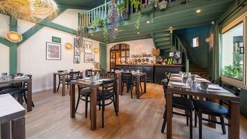 A restaurant with wooden tables and chairs, hanging plants, and a bar area.