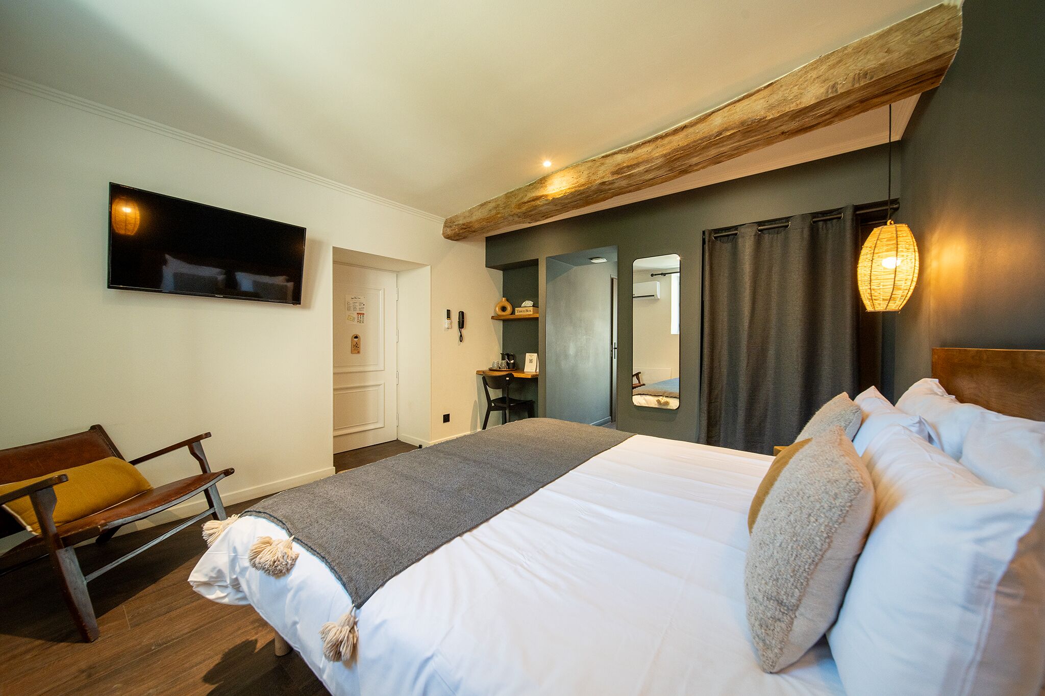 A bedroom with a bed, a wooden bench, a desk, a mirror, and a television.