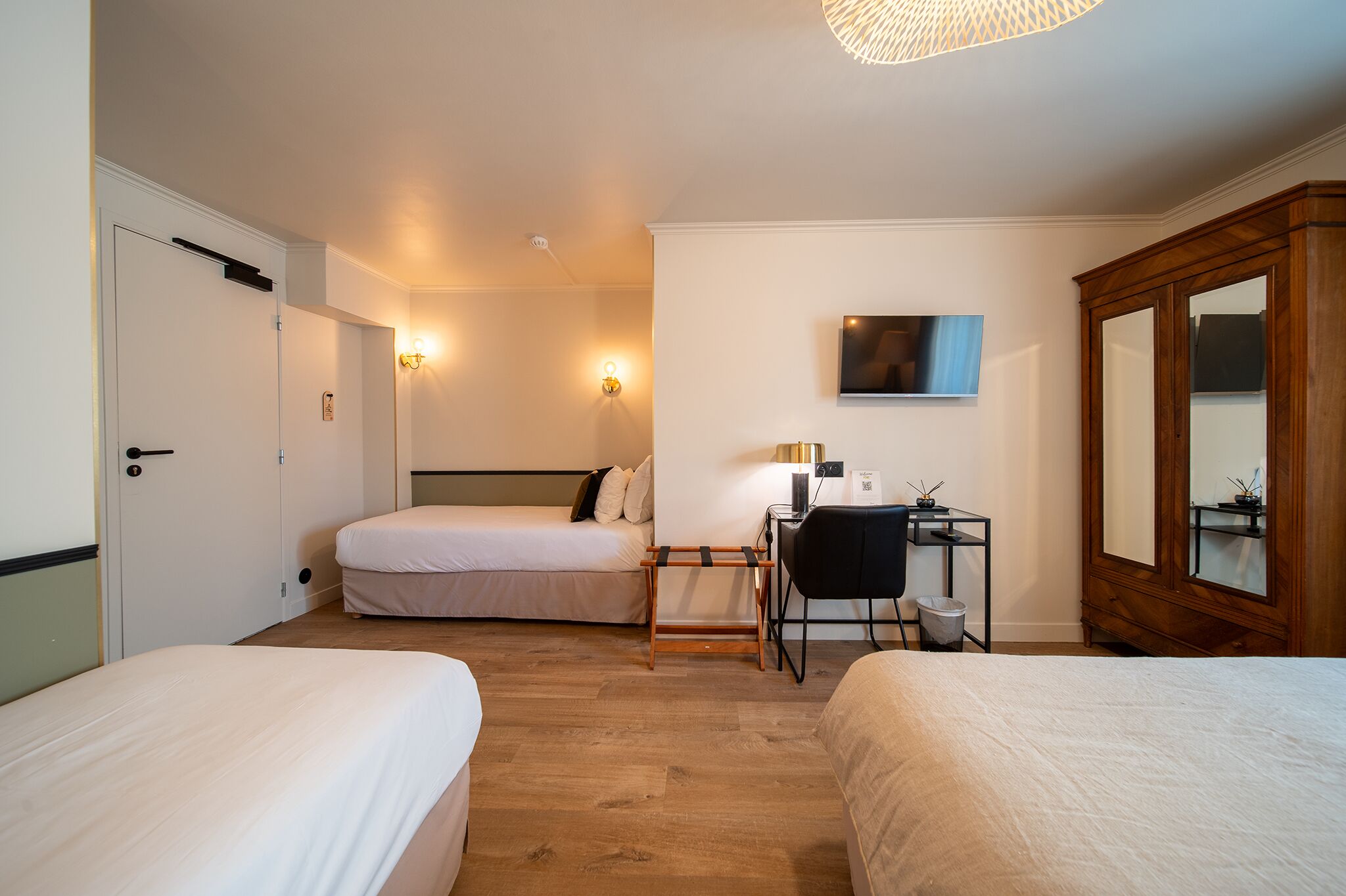 A hotel room with two beds, a desk with a chair, a television, and a large mirror.