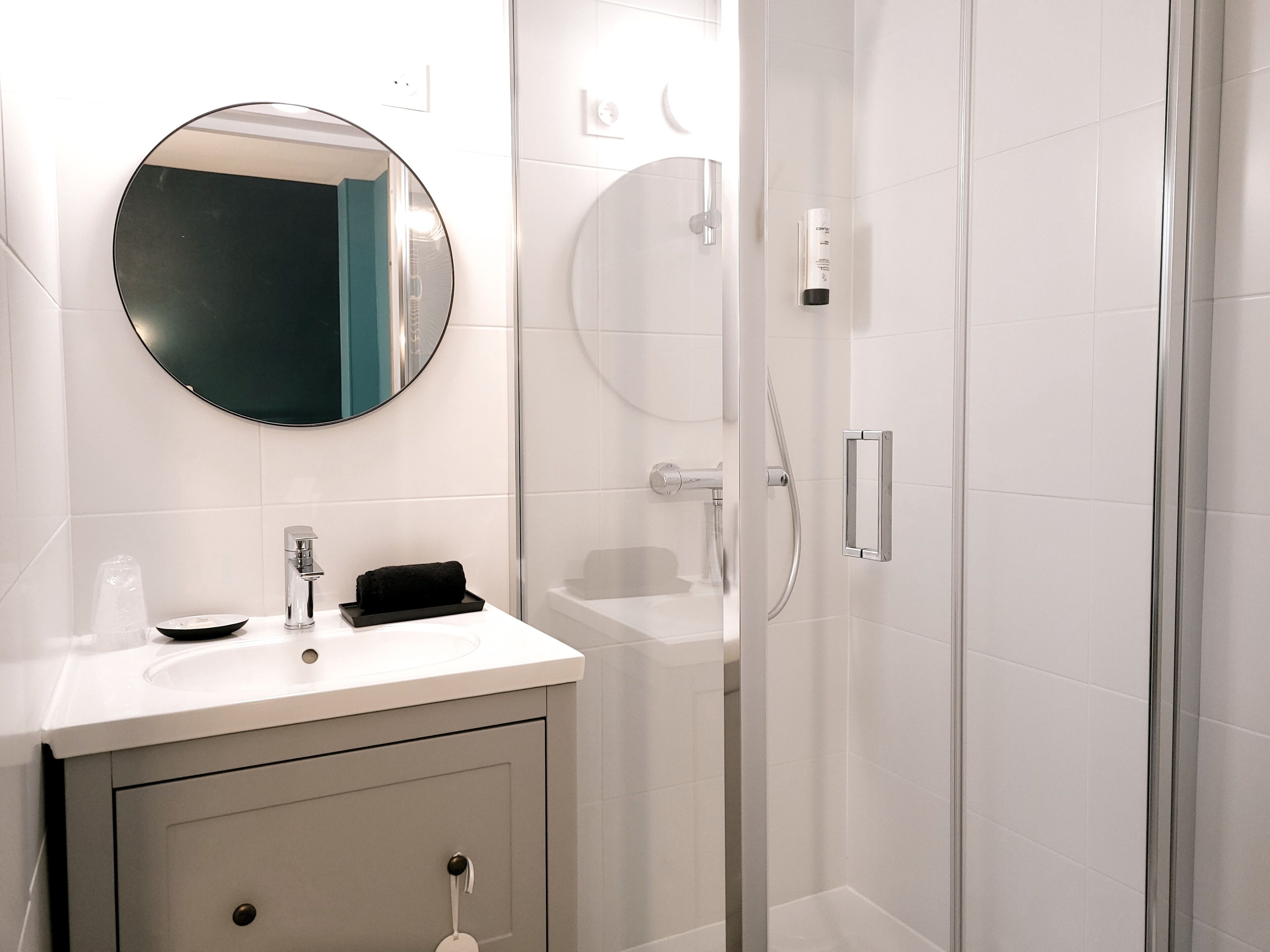 Un baño moderno con un espejo redondo, un lavabo y una ducha con mampara de vidrio.
