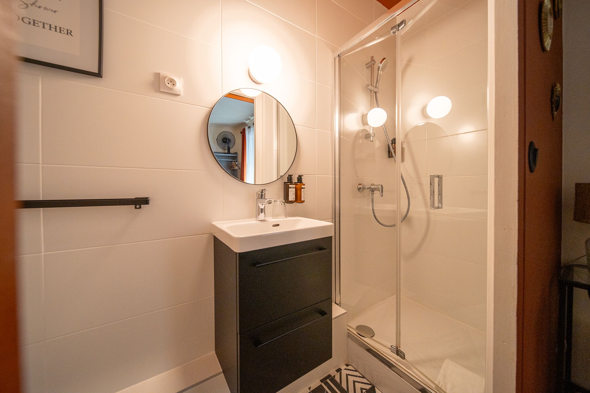 A bathroom with a glass shower enclosure, a sink with a mirror, and a towel rack.