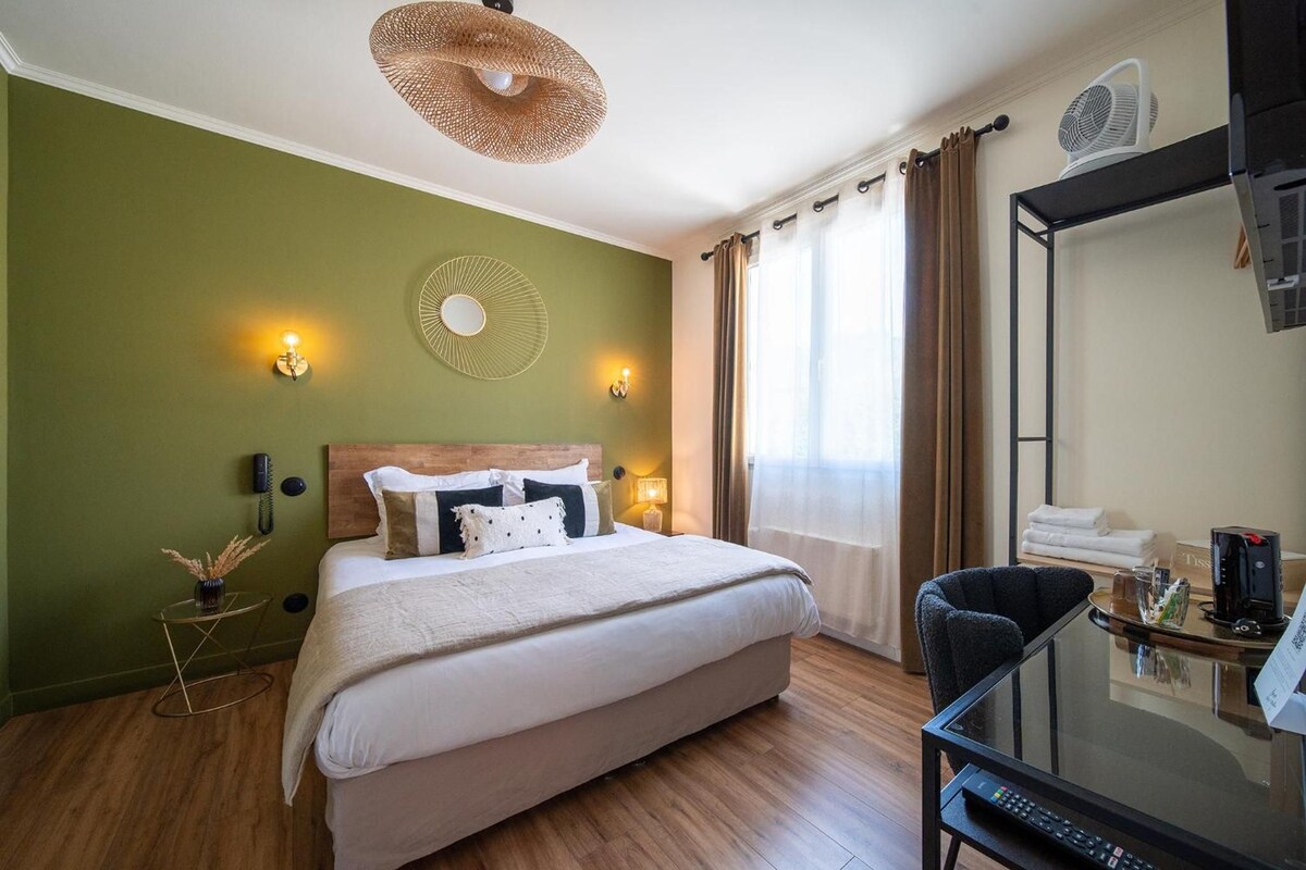 Une chambre d’hôtel comprenant un lit, des lampes de chevet, un miroir, un bureau avec une machine à café et une fenêtre avec des rideaux.