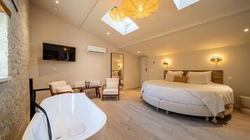 A modern bedroom with a large bed, a bathtub, a TV, and a skylight.