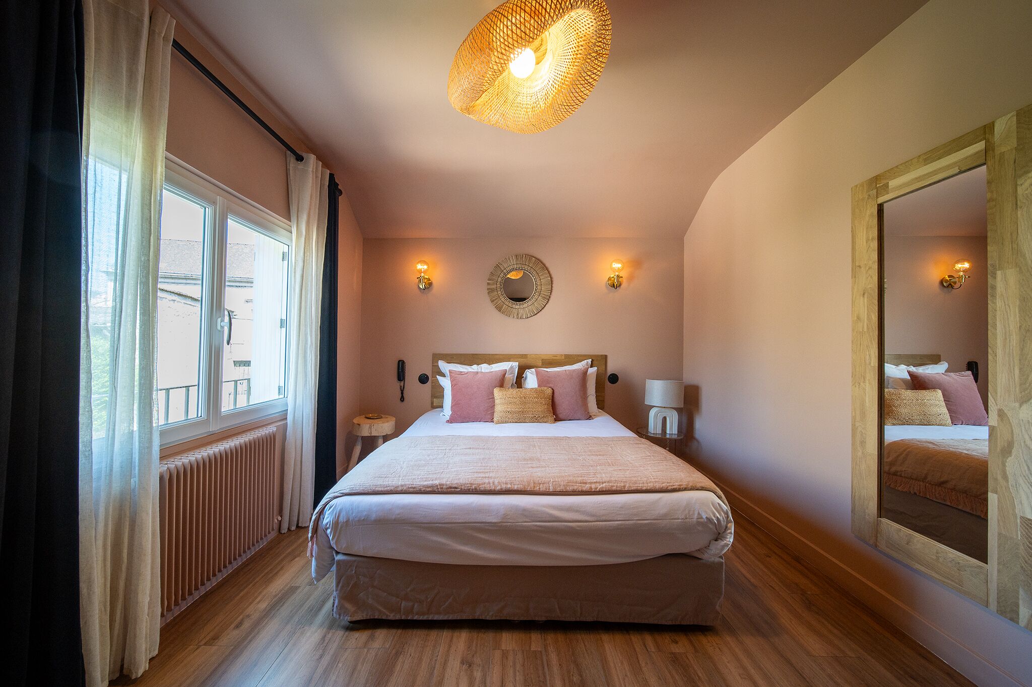 Una camera da letto con un letto grande, uno specchio rotondo a parete e un lampadario.