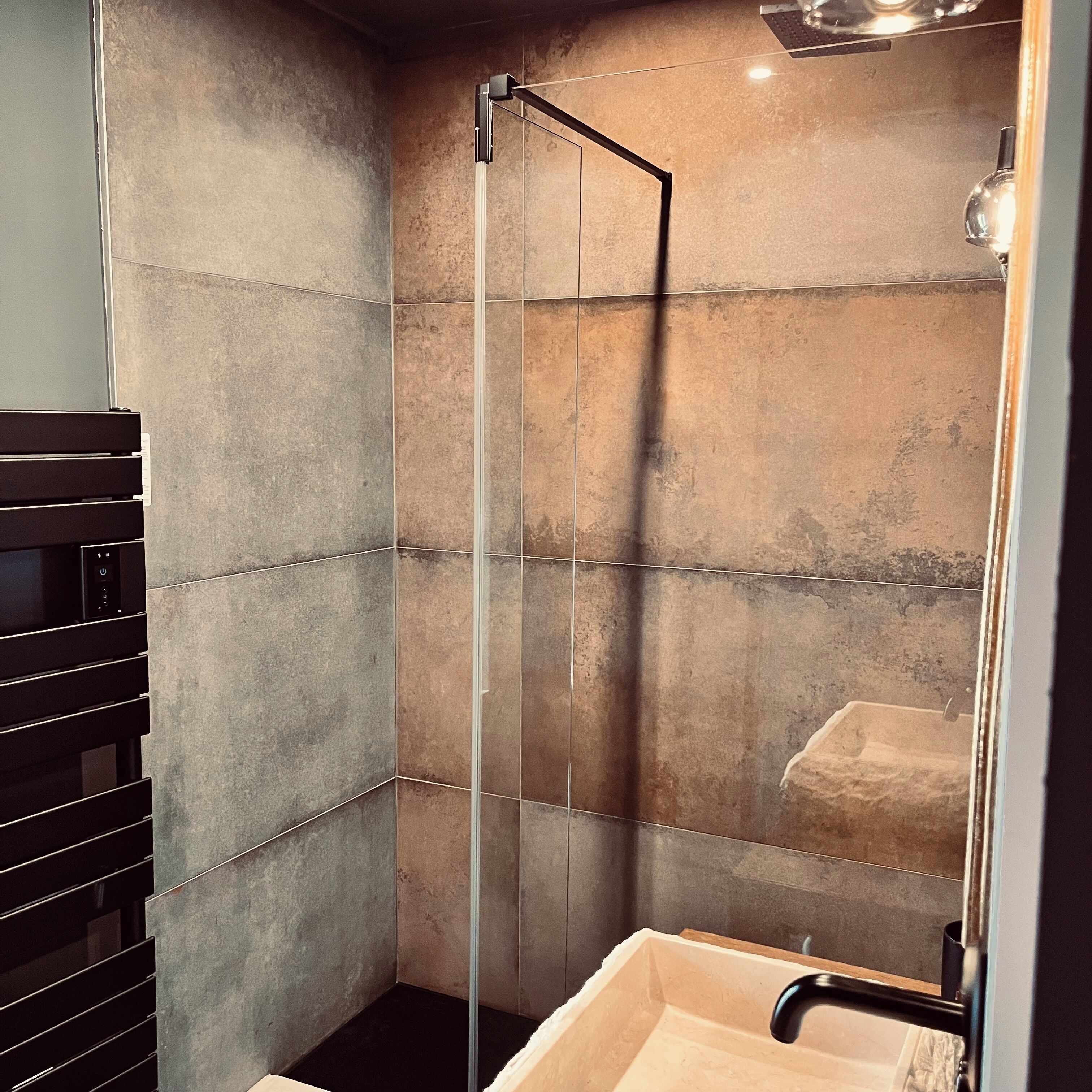 Une salle de bain moderne avec une douche à parois de verre, un porte-serviettes noir et un lavabo beige.