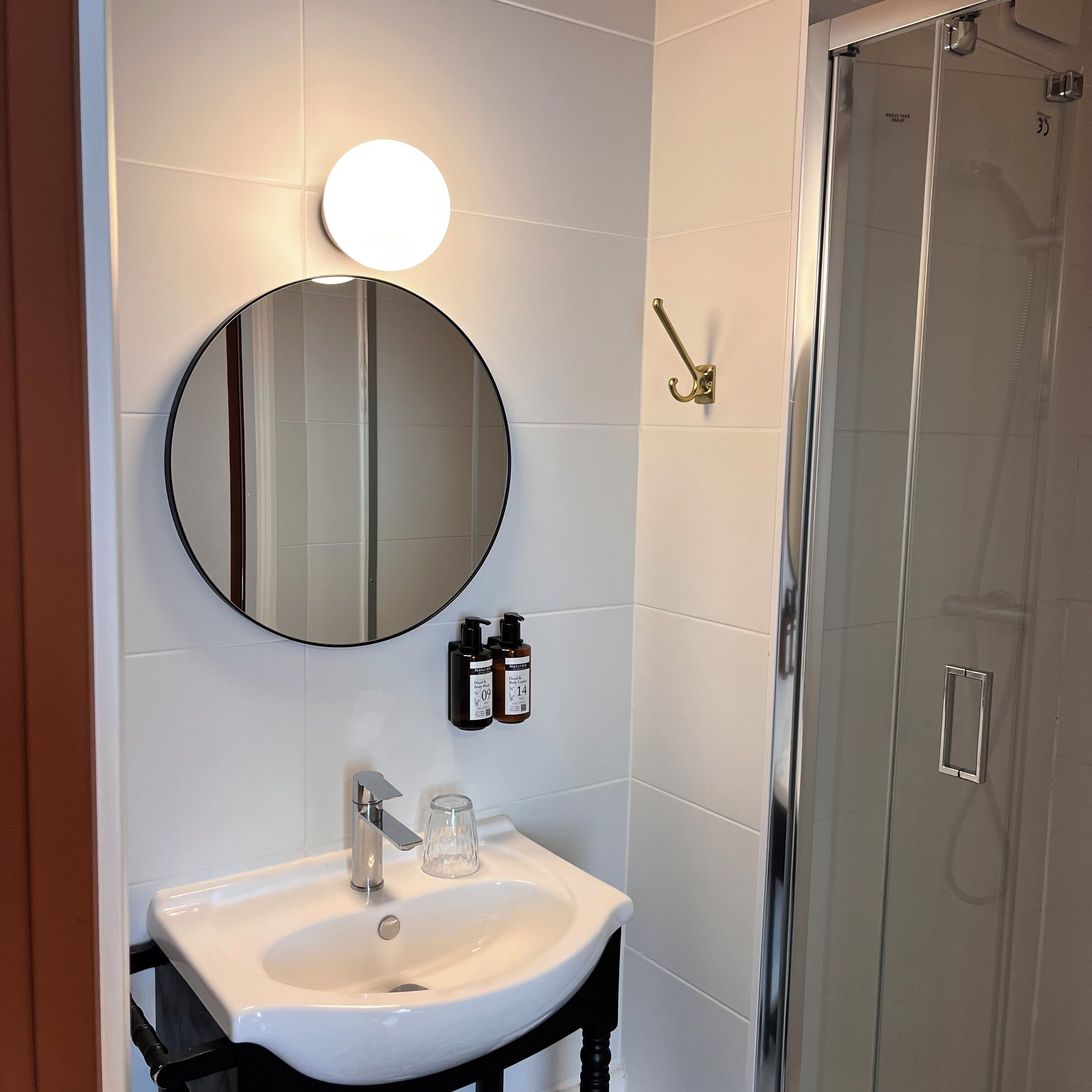 A bathroom with a round mirror, a white sink, and two bottles of shampoo.