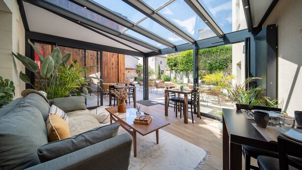 A modern living room with a glass ceiling, wooden furniture, and potted plants. - Hôtel Rive Sud (Chinon)