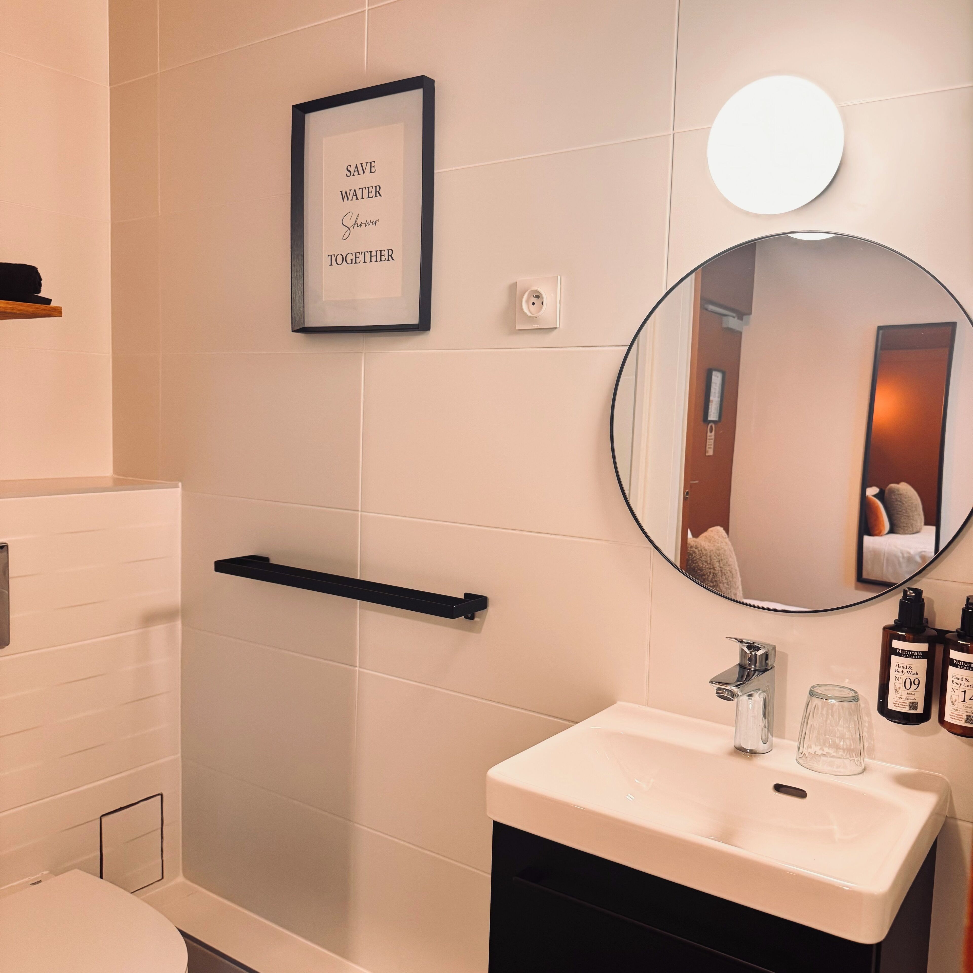 A bathroom with a white sink, a mirror, and a framed sign that reads "SAVE WATER Shower Together".