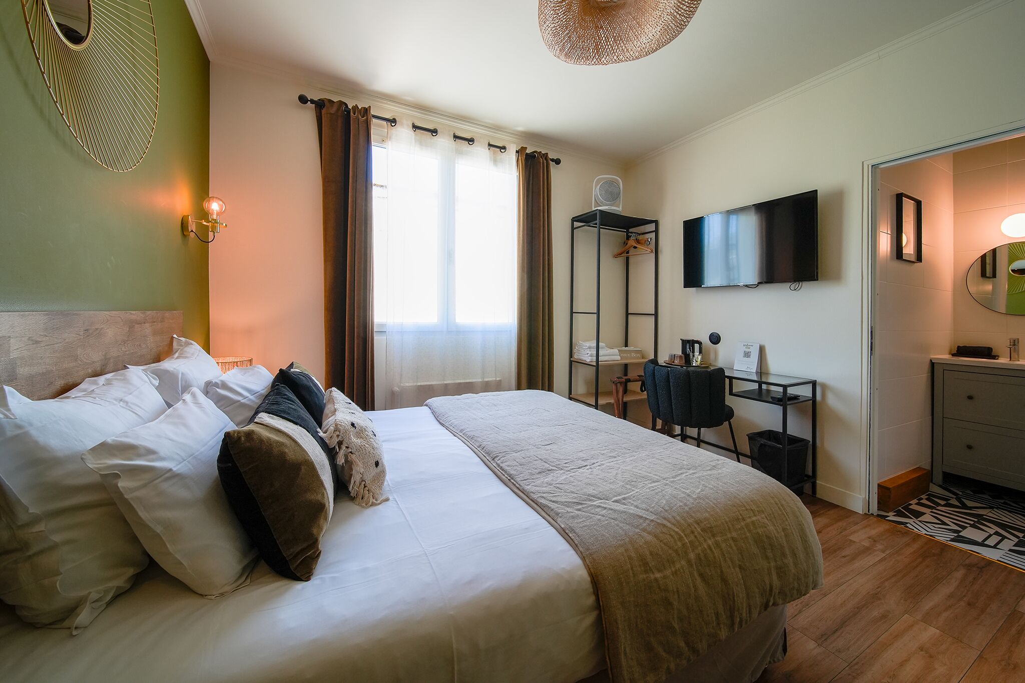 A hotel room with a bed, a desk with a chair, a television, and a wardrobe.