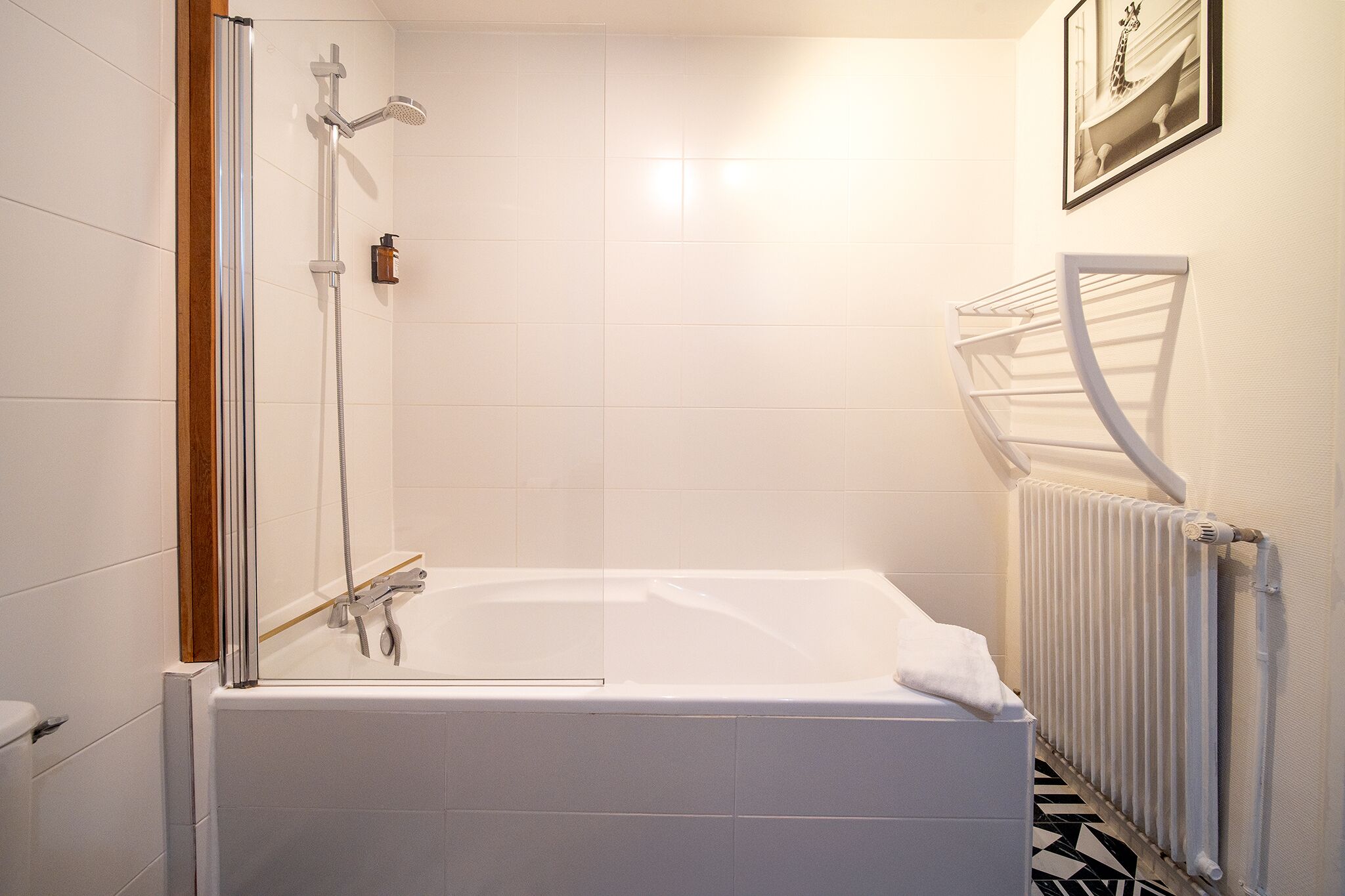 Un baño moderno con ducha acristalada, bañera blanca y suelo con estampado blanco y negro.