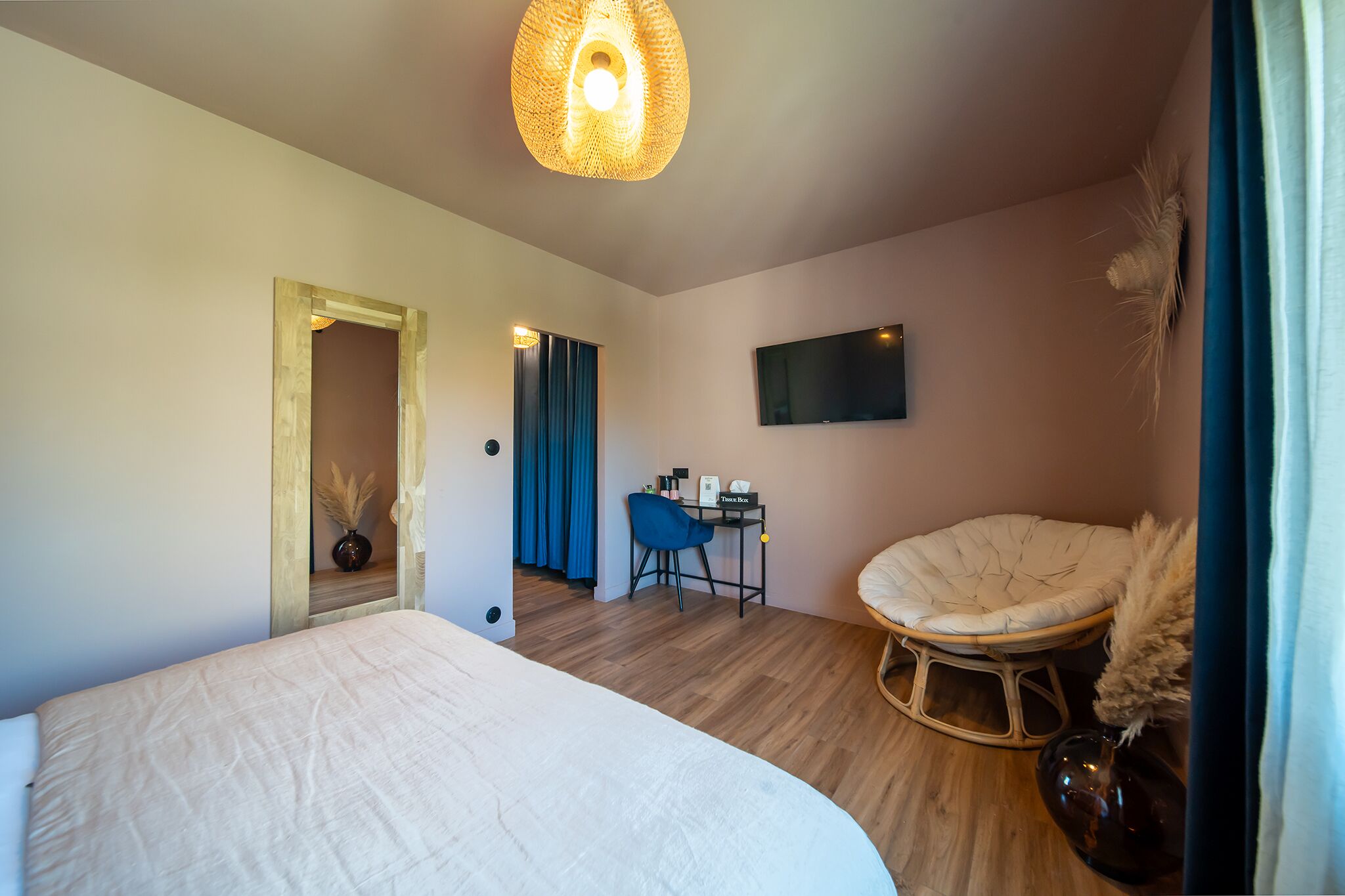 Et moderne hotelværelse med en stor seng, et skrivebord med stol, et fjernsyn ophængt på væggen og en dekorativ lænestol.