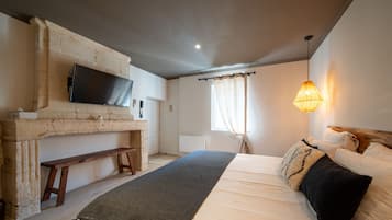 Un dormitorio con una cama, un banco, un televisor montado en una pared de piedra y una ventana con cortinas.