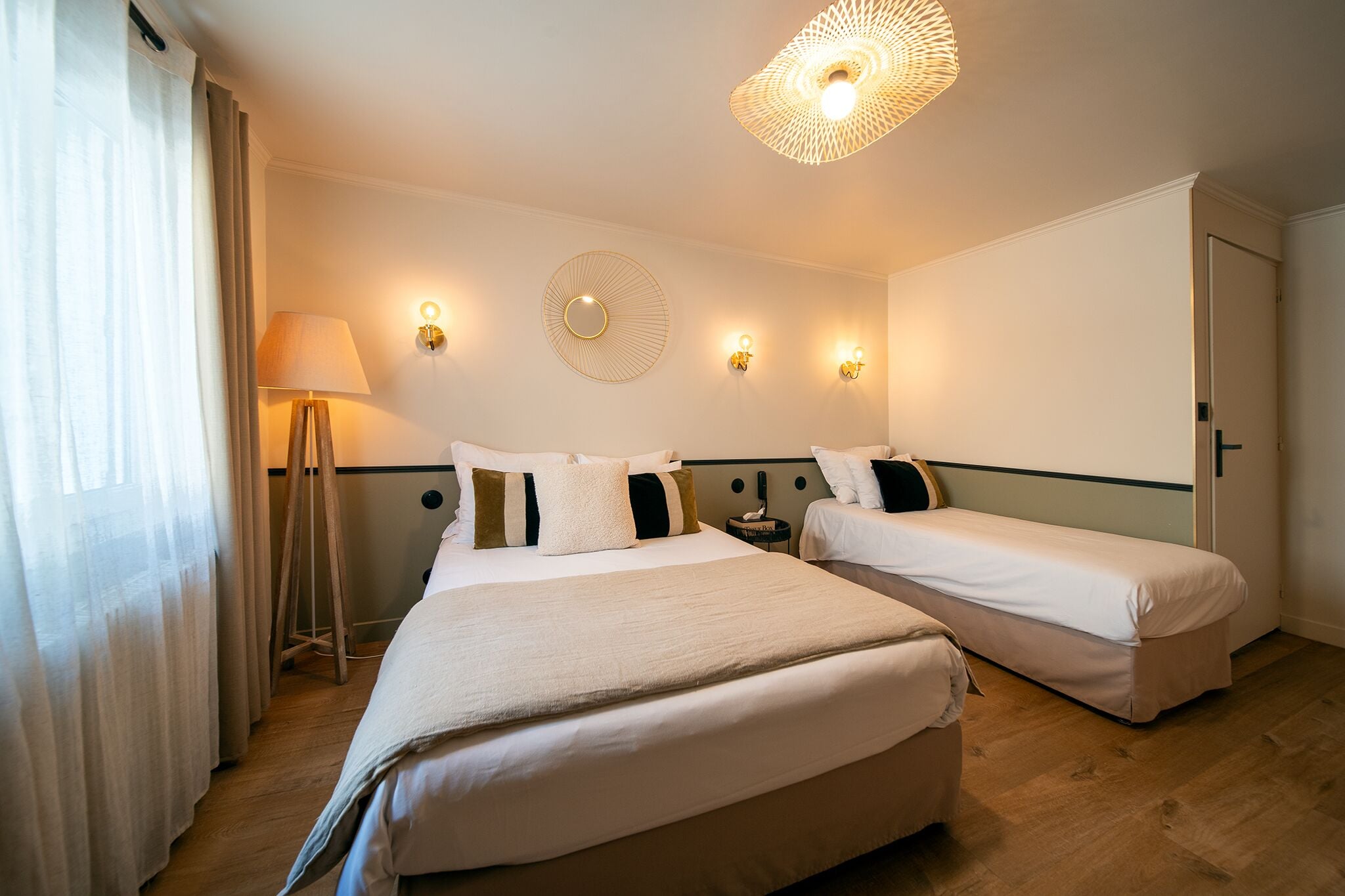 Habitación de hotel con dos camas, una lámpara de pie, apliques de pared y un candelabro en el techo.
