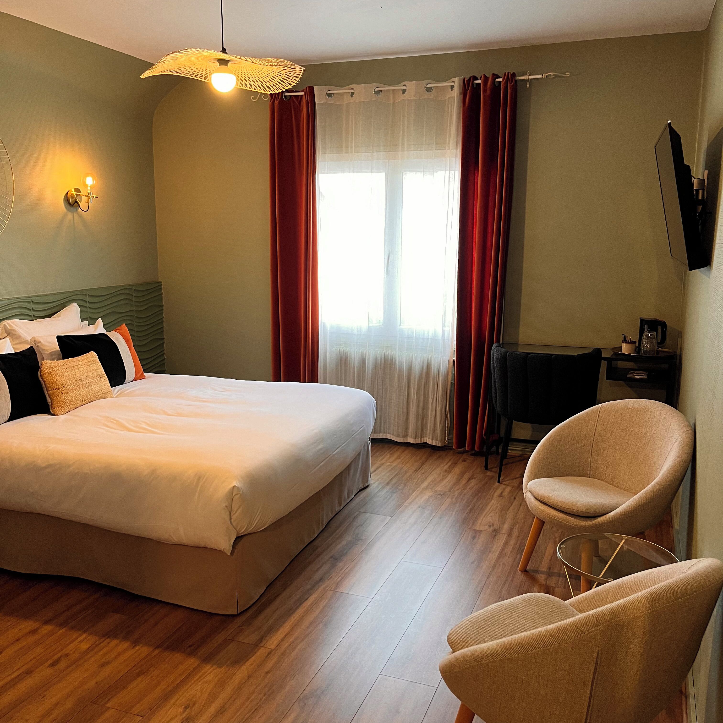 Una habitación de hotel con cama, una silla, un escritorio y una ventana con cortinas.
