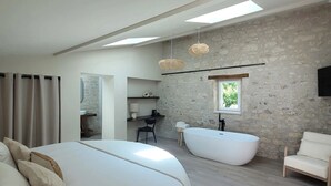 A modern bedroom with a large bed, a separate bathroom with a freestanding bathtub, and a small desk area. - Hôtel Rive Sud (Chinon)