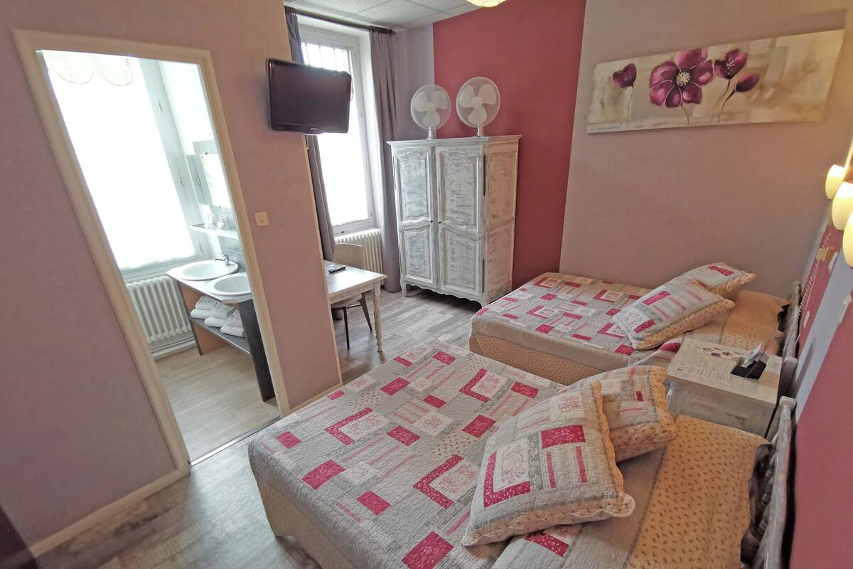 A bedroom with two beds, a desk, a chair, a TV, and a radiator.
