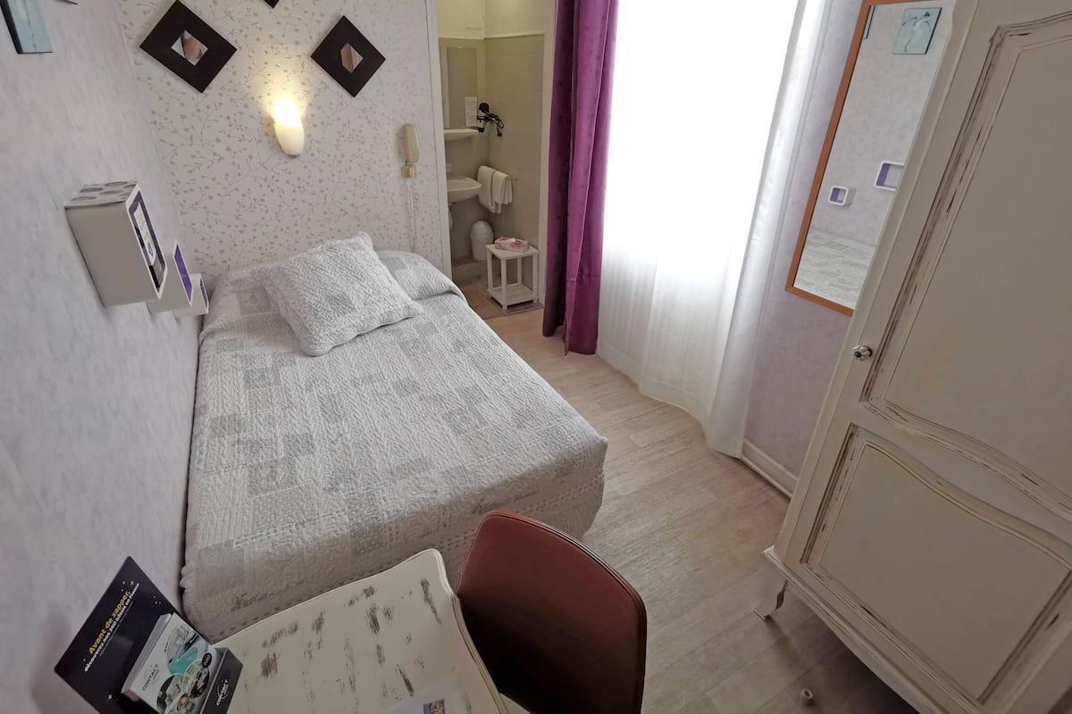 A hotel room with a bed, a desk, a chair, a wardrobe, and a bathroom visible through an open door.