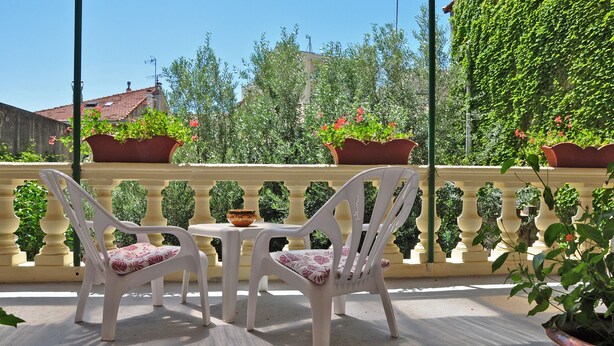 A terrace with white plastic chairs and a table, surrounded by potted plants and a decorative balustrade. - Hôtel Select (Salon-de-Provence)