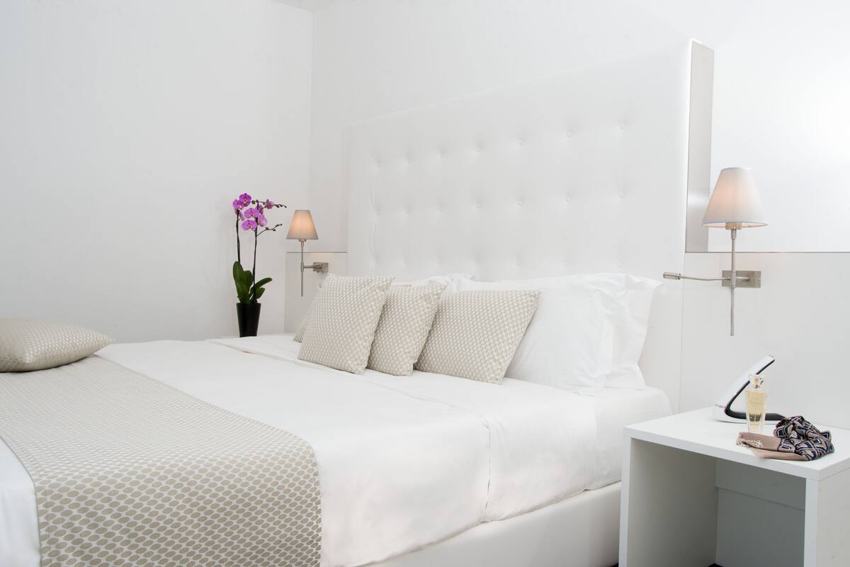 A neatly made bed with a white headboard, a bedside table with a lamp, and a potted orchid.