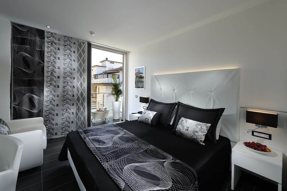 A modern bedroom with a large bed, a bedside table with a lamp, and a view of the outside.