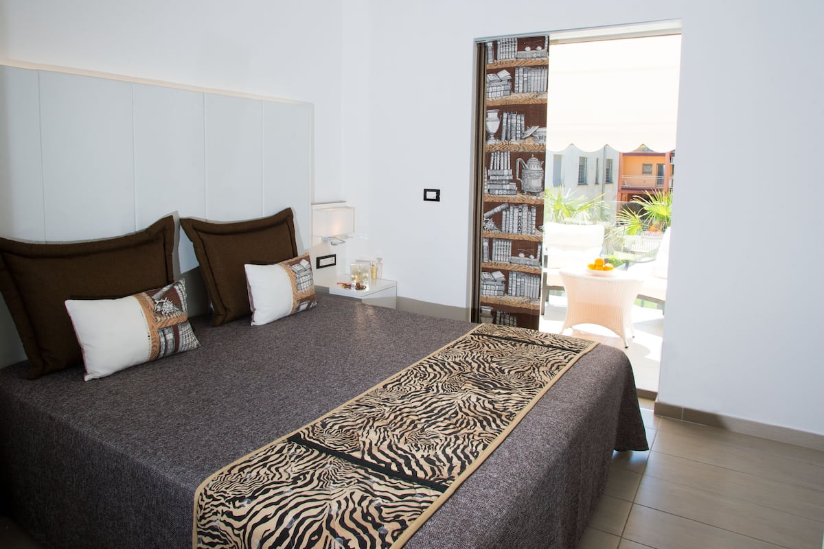A bedroom with a large bed, a bookshelf, and a view of the outside.