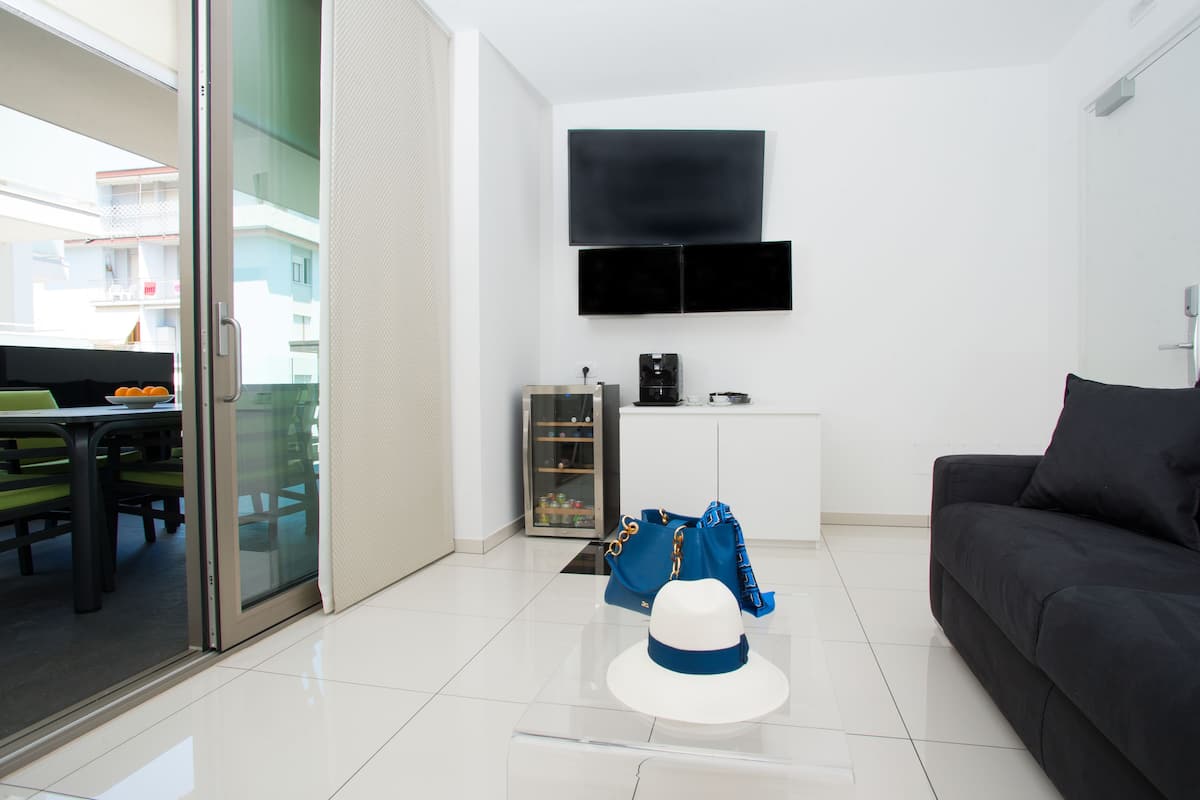 A modern living room with a flat-screen TV, a sofa, a coffee machine, and a dining area with a table and chairs.