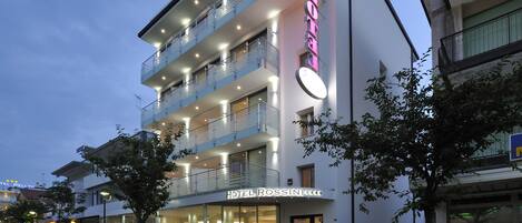 A multi-story hotel with balconies, a well-lit entrance, and a visible sign reading "HOTEL ROSSINI".