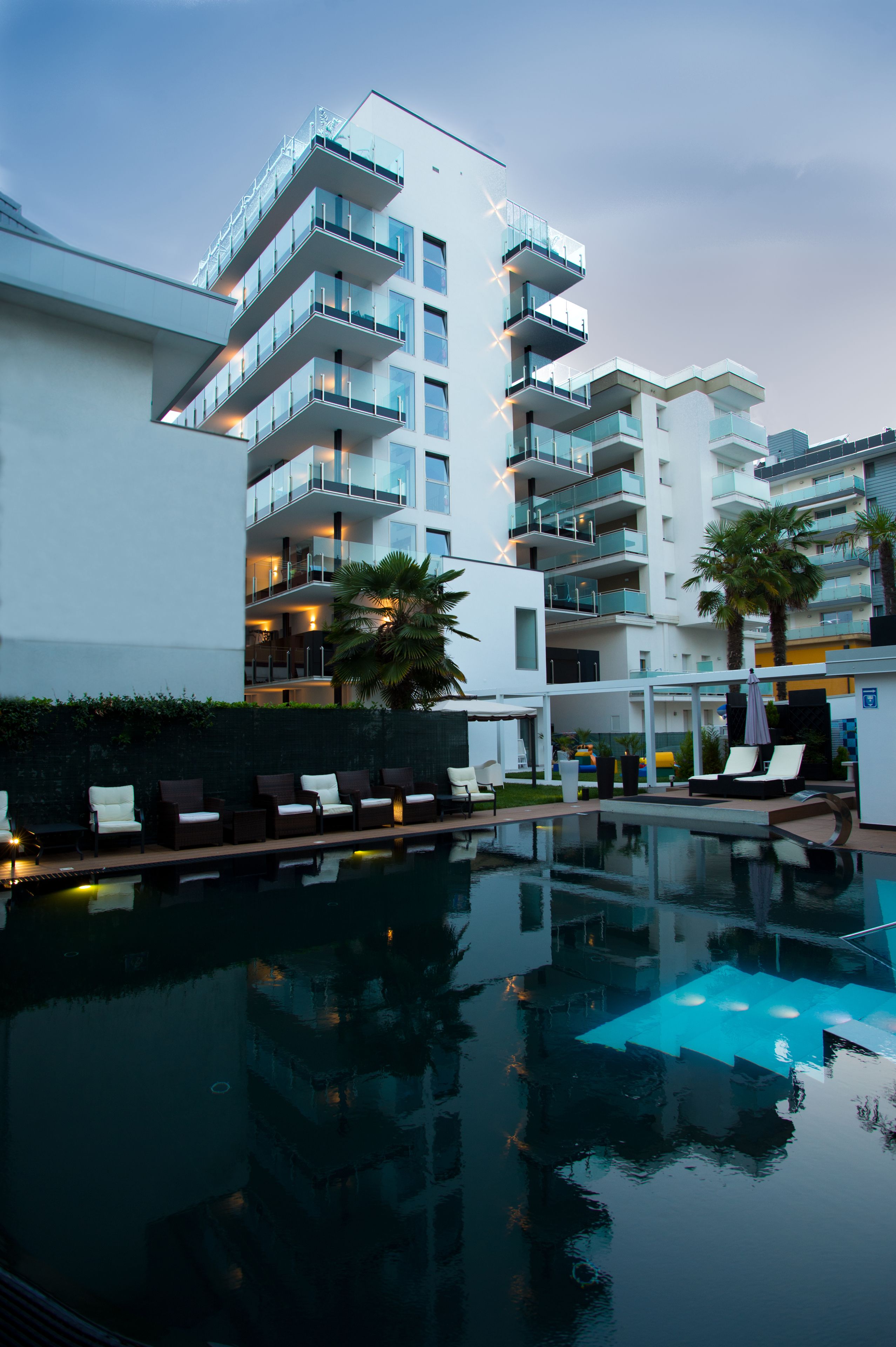 A modern hotel with a pool, multiple balconies, and lounge chairs.