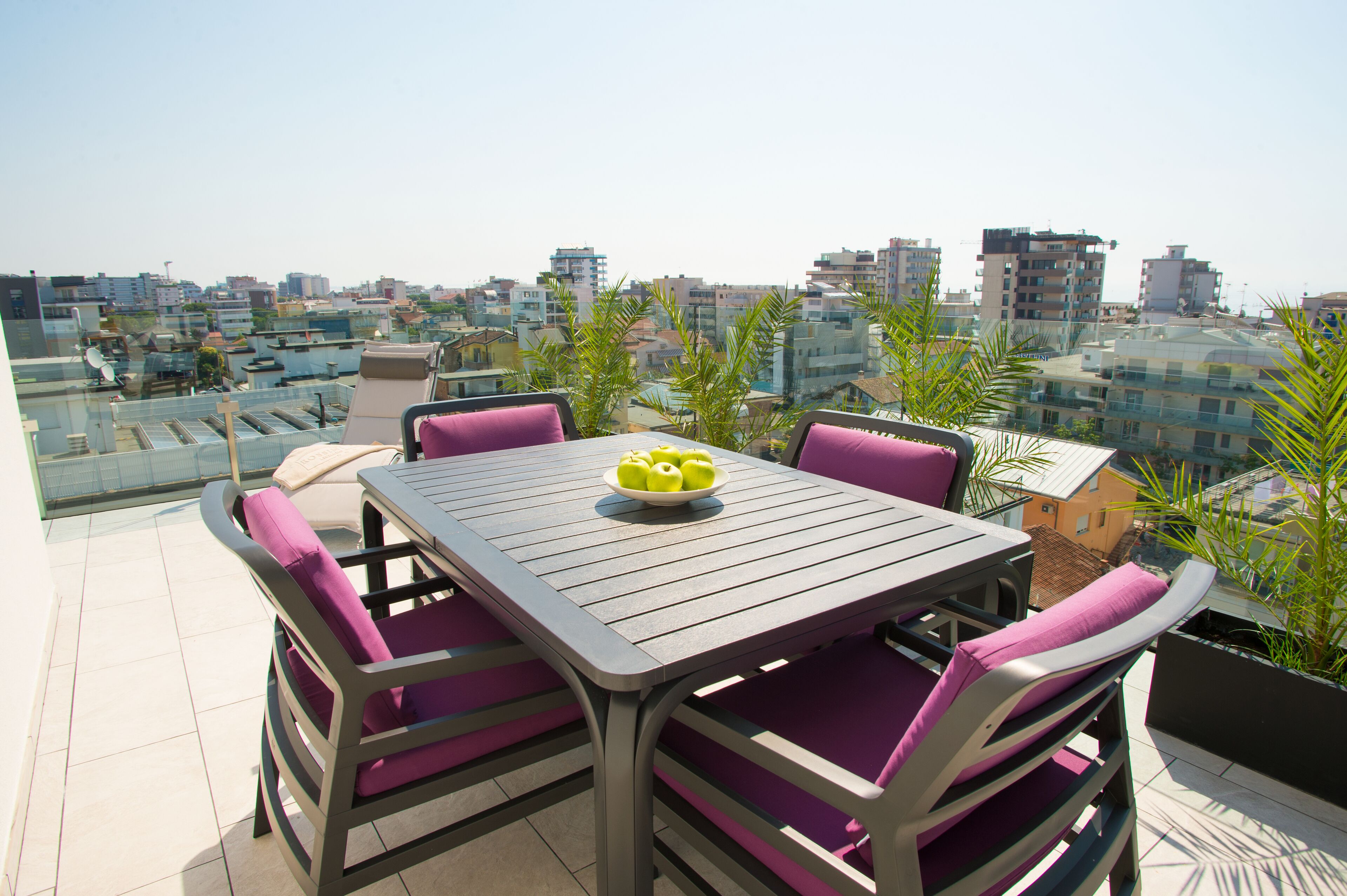 A rooftop terrace with a table and chairs, a bowl of fruit, and a city view.