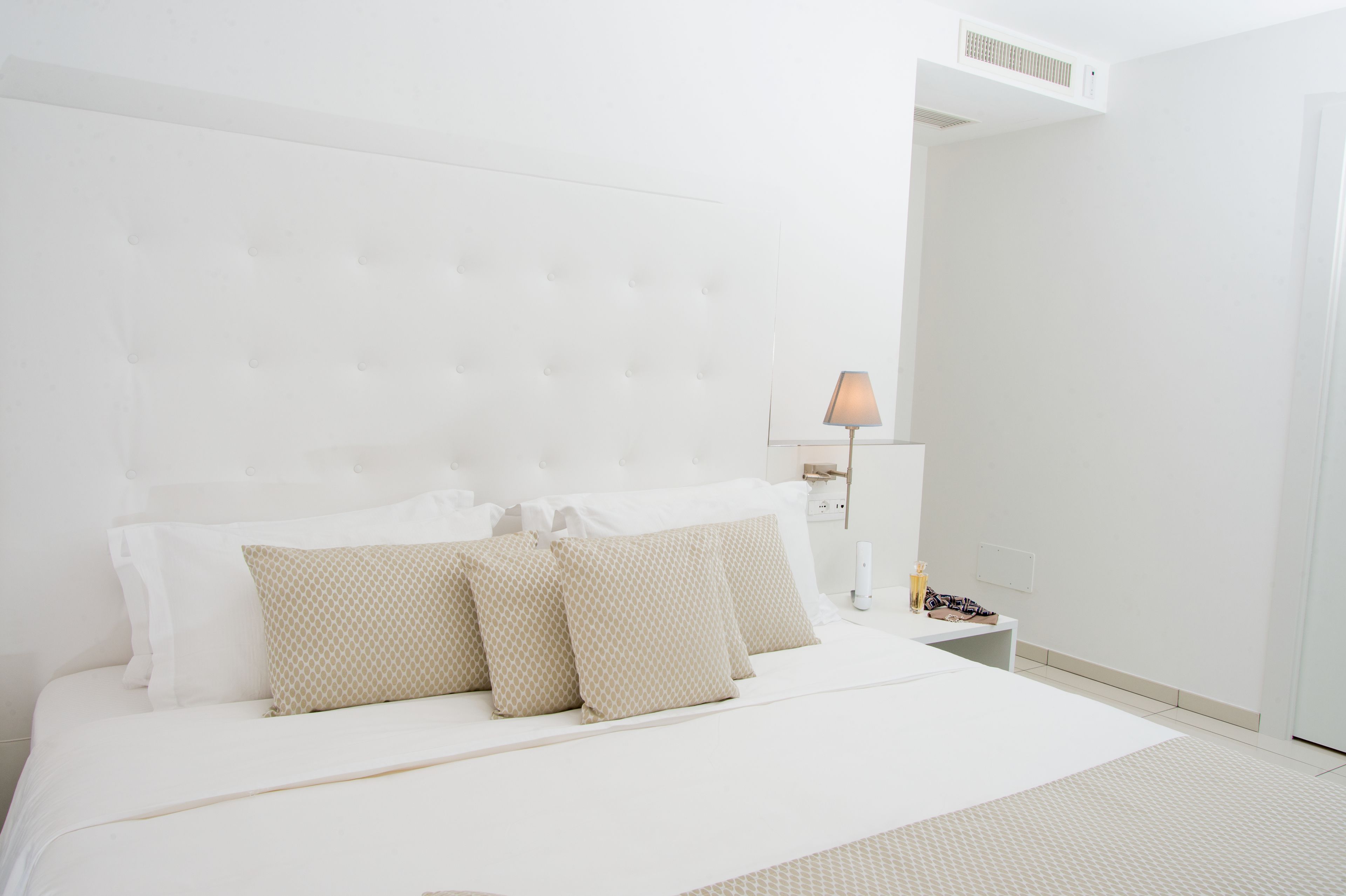 A modern hotel room with a large bed, a bedside table with a lamp, and a small nightstand.