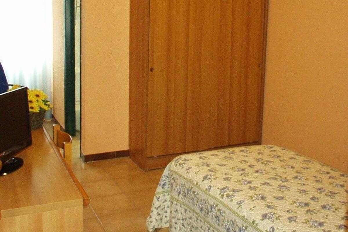 Un dormitorio con un armario de madera, una cama con colcha floral, un escritorio con computadora y una ventana con cortinas.