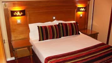 Een hotelkamer met een houten hoofdeinde, een enkel bed met witte lakens, een gestreept plaid en twee bedlampen.
