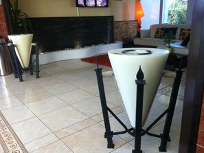 A modern lobby with a tiled floor, a fireplace, a sofa, and a small table with a candle. - Hôtel du Val de Seine (Mantes-la-Jolie)