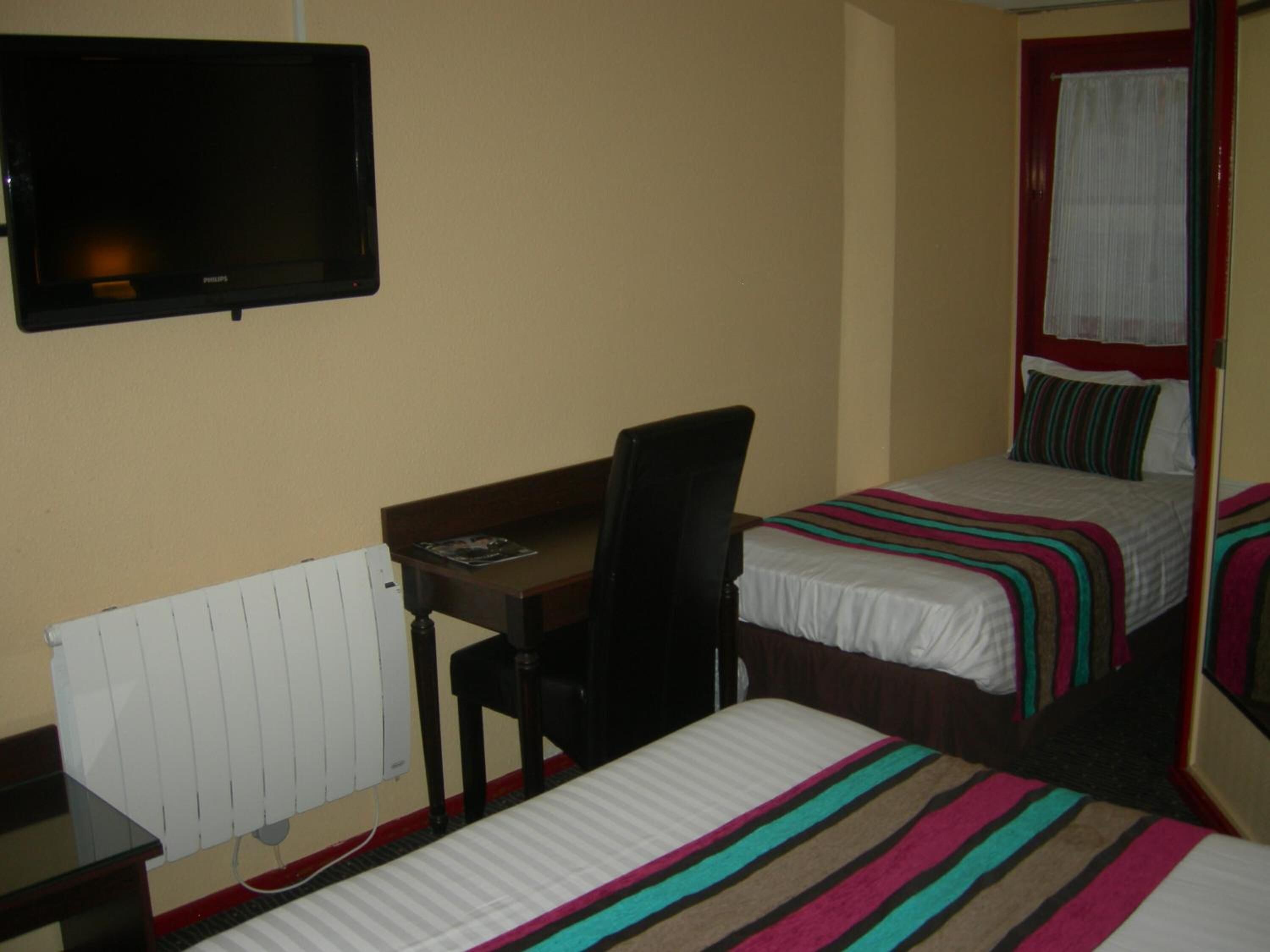 A hotel room with a bed, a desk, a chair, a TV, and a window with curtains.