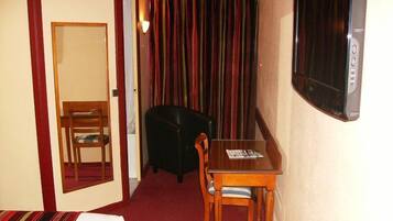Una habitación de hotel con una cama, una mesa de madera con dos sillas, un sillón negro, una cortina a rayas y un televisor fijado a la pared.