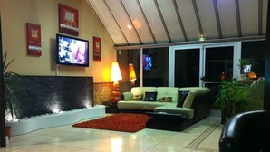 A modern living room with a sofa, a red rug, and a TV mounted on the wall. - Hôtel du Val de Seine (Mantes-la-Jolie)
