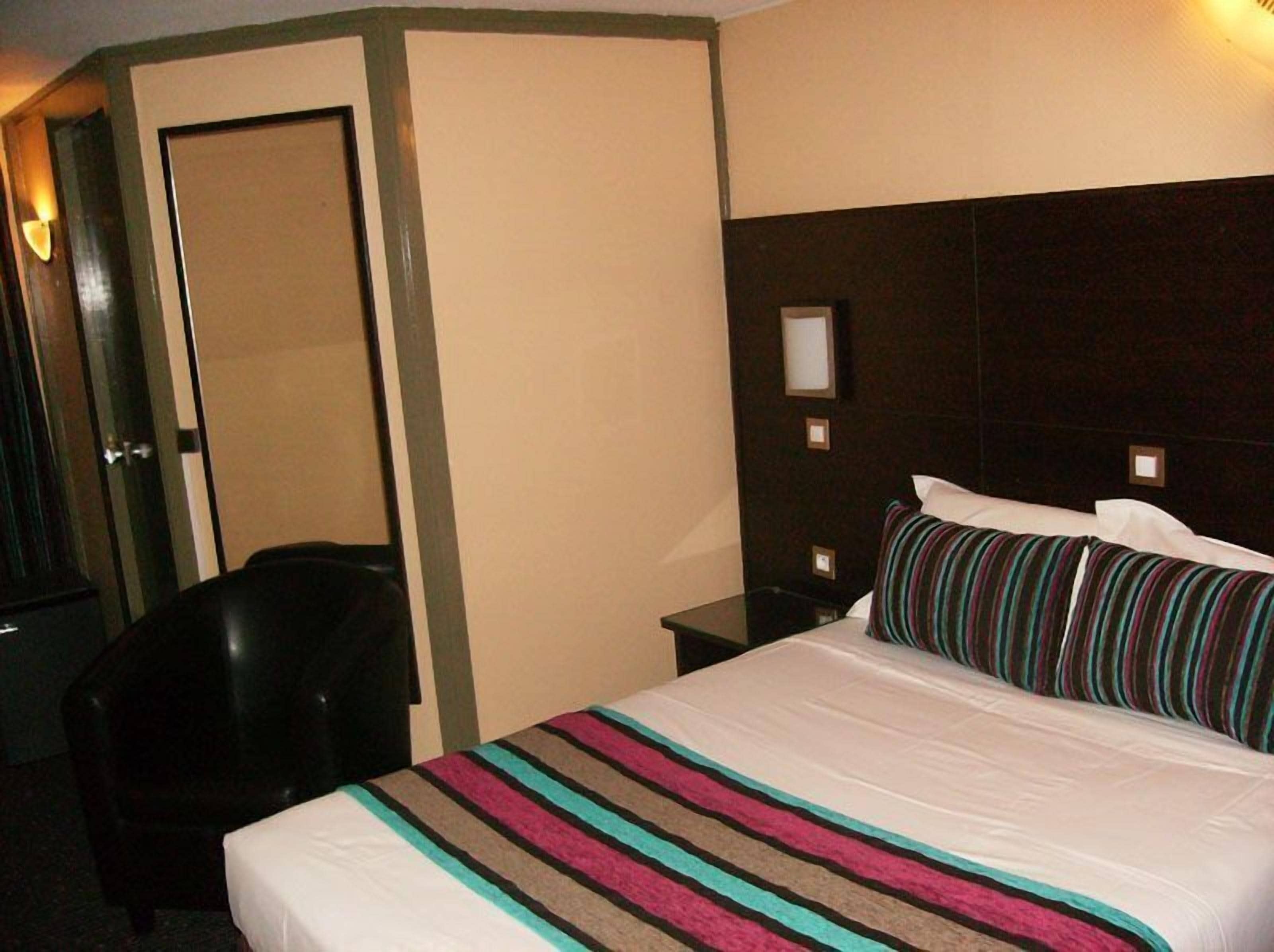 Una habitación de hotel con una cama, una silla, una mesita de noche y una puerta.