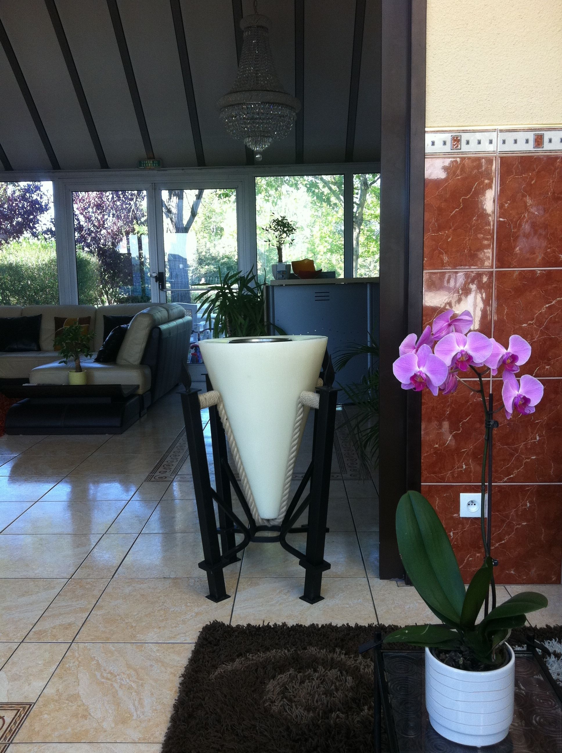 Uma sala de estar moderna com um sofá, uma cadeira branca, uma orquídea em vaso e um chão ladrilhado.