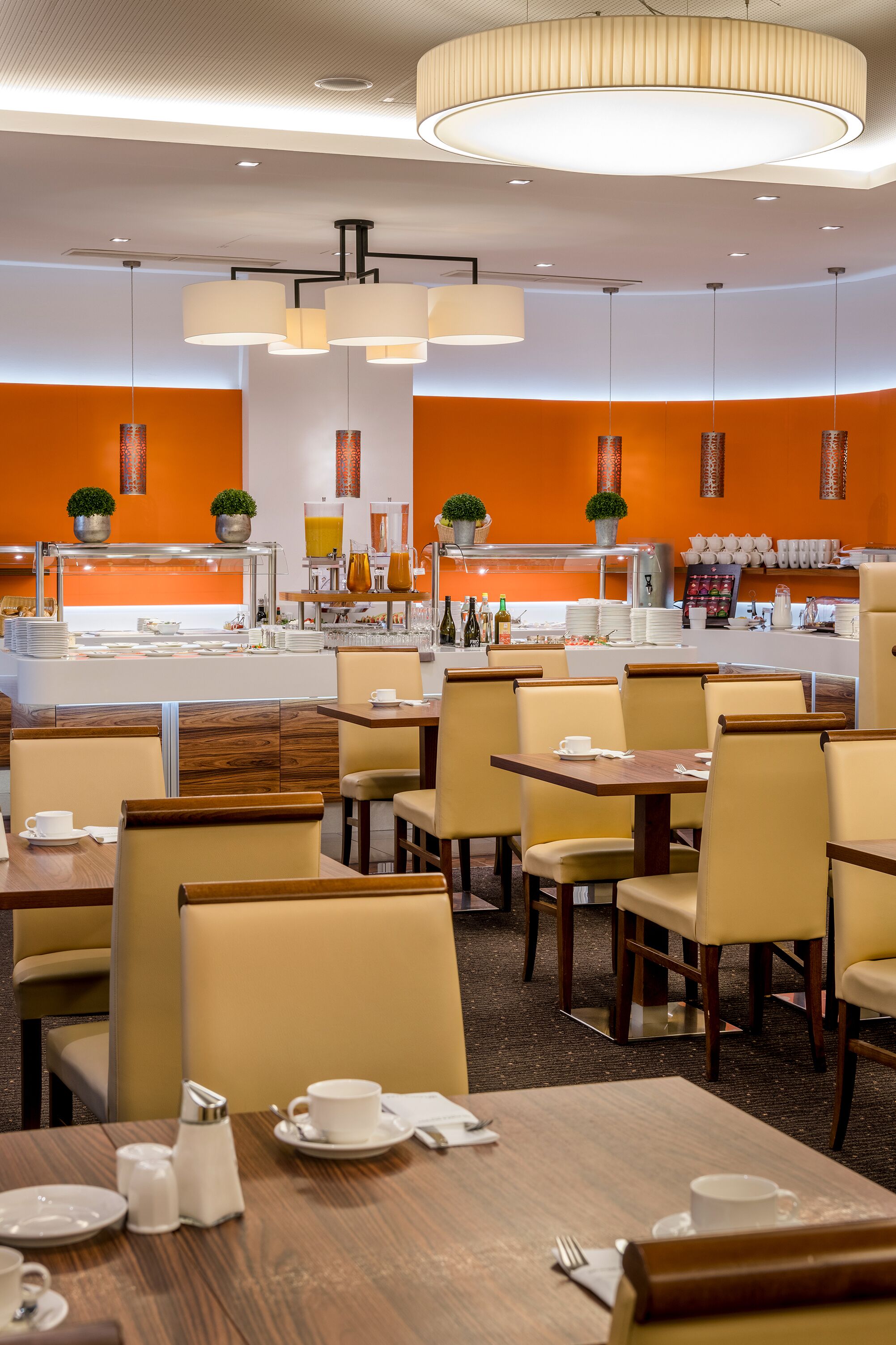 Een moderne eetruimte met meerdere tafels en stoelen, een centraal buffet en hangende lichtarmaturen.
