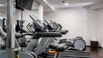 A row of treadmills in a gym with a flat-screen TV mounted on the wall.