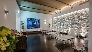 Un moderno cuarto de spa con pared de piedra, sillones de descanso, un amplio cuadro abstracto y un sofá de mimbre.